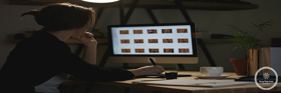 Back view image of concentrated young lady designer sitting indoors using computer and graphics tablet.