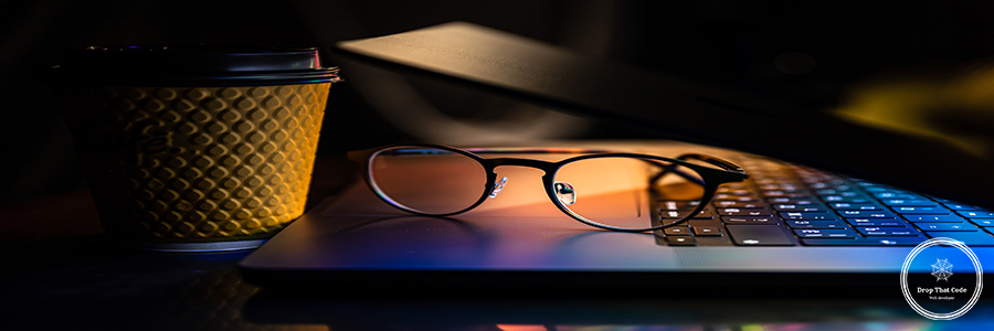 A laptop half closed in the dark with colourful glow, glasses and paper cup. Night work, Stock exchange financial market price candles graph data pattern analysis concept.