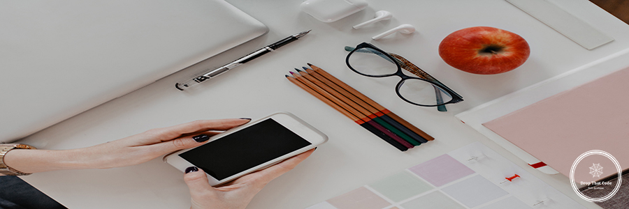 Flat lay. Womans hands holding iPhone on background of pencils, glasses, MacBook. Website Design for Small Business